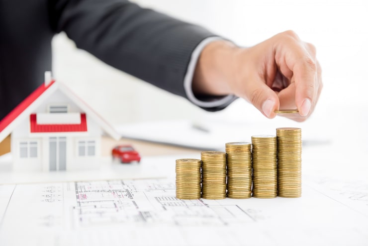 Coins stacked beside a model house on plans, showing the price and cost of a home at Serene Sagara